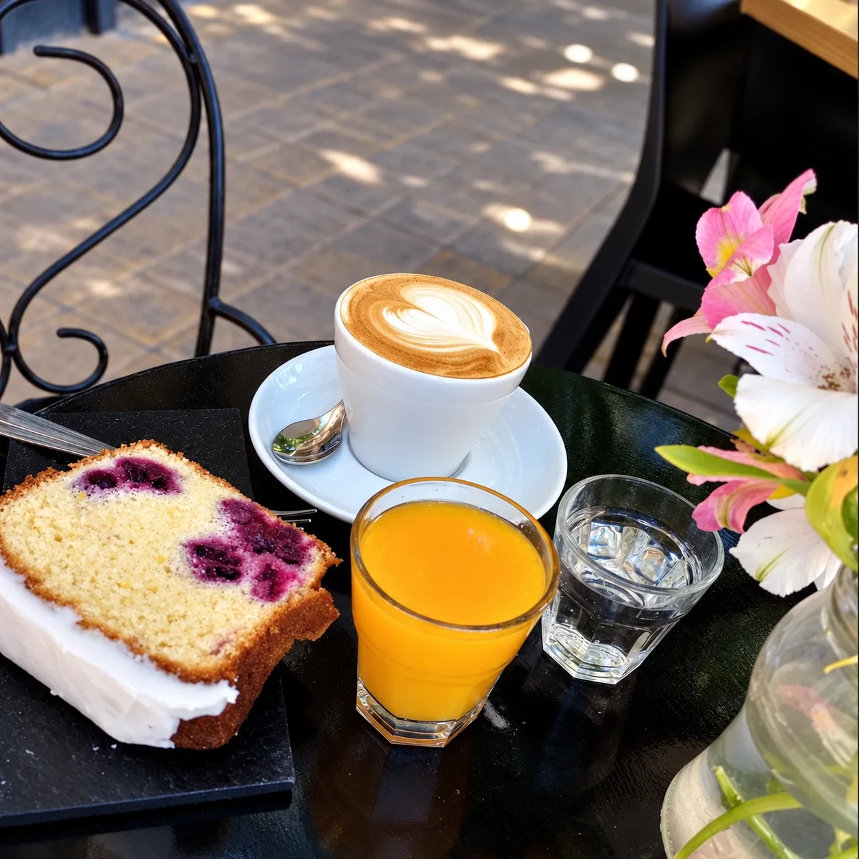 Una porción de budín, un café y un jugo de naranja en una mesa de la vereda