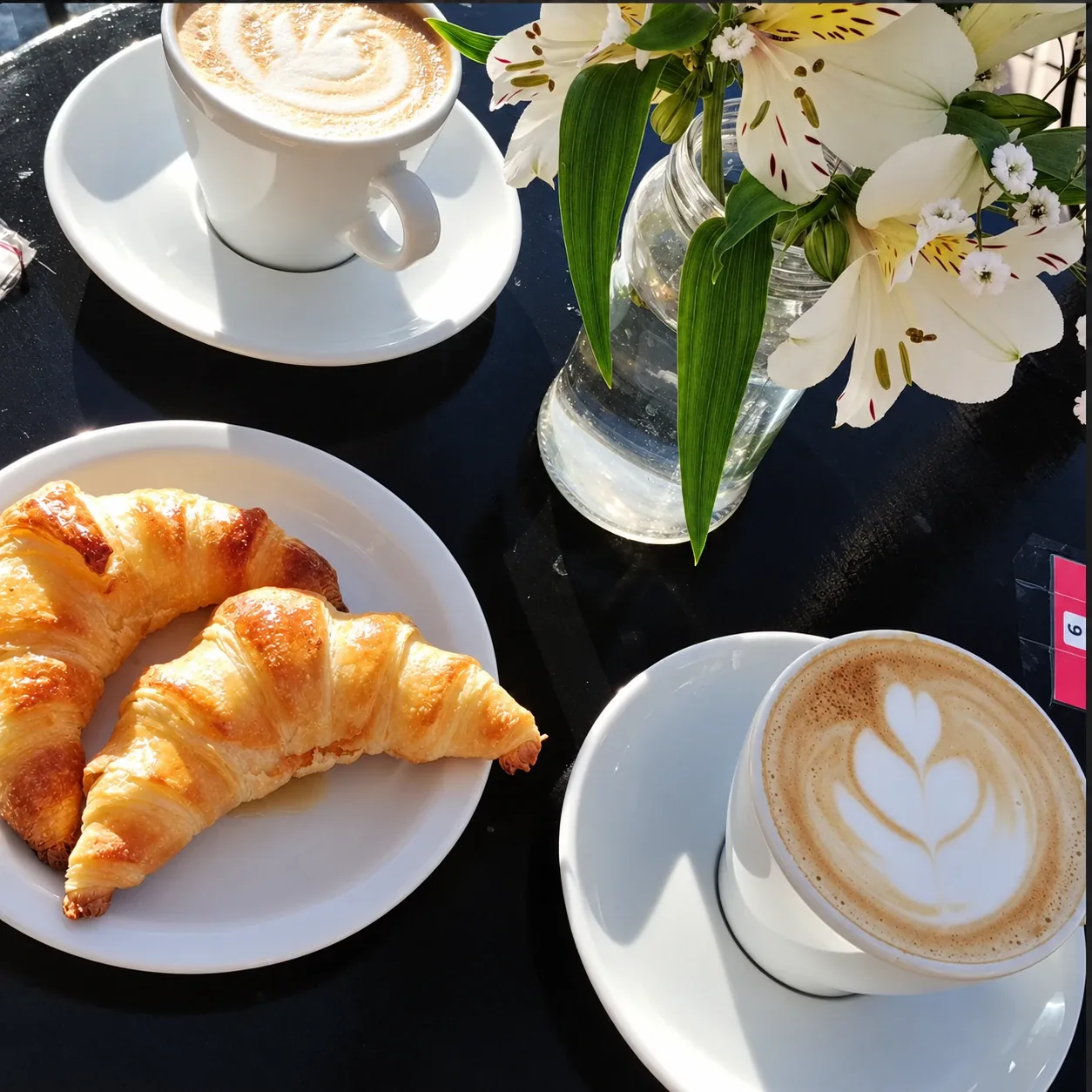 Dos cafés con leche y medialunas en una mesa, con flores
