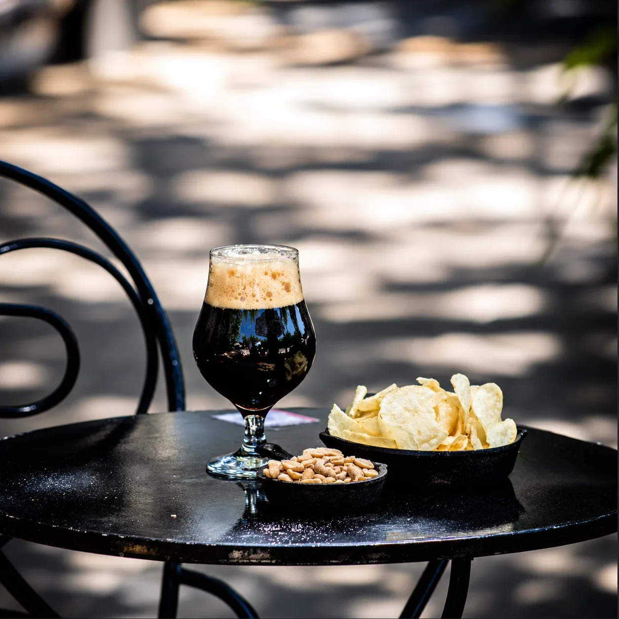 Una cerveza negra con papas fritas y maní, en una mesa de la vereda