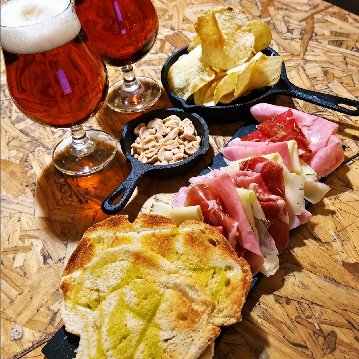 Dos cervezas con una picada de jamón crudo, jamón cocido y queso, pan tostado, papas fritas y maní